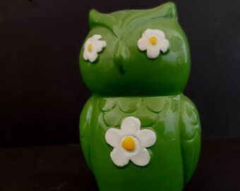 May include: A green ceramic owl figurine with white flowers and yellow centers. The owl has a glossy finish.