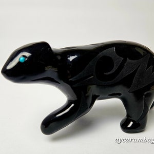 May include: Black obsidian bear figurine with a turquoise eye inlay and intricate carved details. The bear is standing on all fours and has a stylised design on its back.