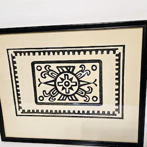 May include: Black and white geometric design print in a black frame. The design features a central starburst with radiating lines and a border of repeating patterns.