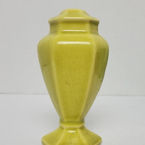 Puede incluir: Un salero de cerámica amarillo con base hexagonal y parte superior redondeada.