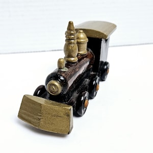 Könnte beinhalten: Ein Holzspielzeugzug mit braunem Körper, goldenen Akzenten und schwarzen Rädern. Der Zug hat eine goldfarbene Front, einen Schornstein und ein Dach. Dieser dekorative Zug ist ein klassisches Spielzeug.