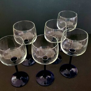 May include: Six clear glass wine glasses with blue stems. The glasses are arranged in a circle on a dark surface.