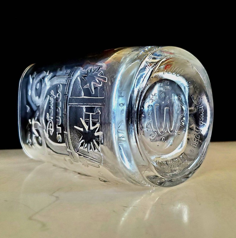 May include: A clear glass cup with a design etched into the side. The design features the words "Disney Studios" and a starburst. The bottom of the cup has the words "Disney World" etched into it.