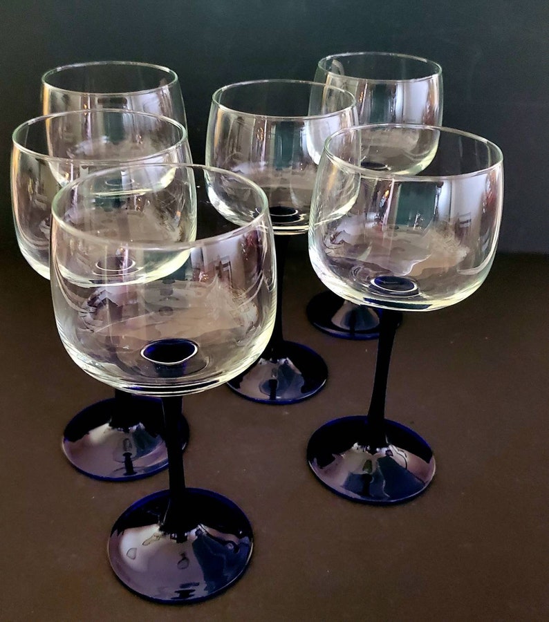May include: Six clear glass wine glasses with blue stems and bases. The glasses are arranged in a semi-circle on a dark surface.