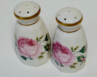 Puede incluir: Un par de saleros y pimenteros de cerámica blanca con ribete dorado y diseño floral de rosas rosas.