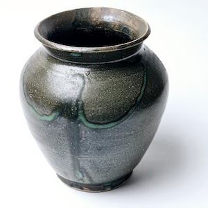Puede incluir: Un jarrón de cerámica gris oscuro con un esmalte verde. El esmalte tiene un efecto de goteo, creando un patrón único.