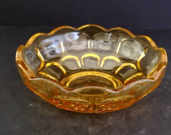 May include: Amber-coloured glass bowl with a scalloped rim. The bowl has a decorative pattern on the exterior and a clear interior. The bowl is likely vintage and suitable for serving or display.