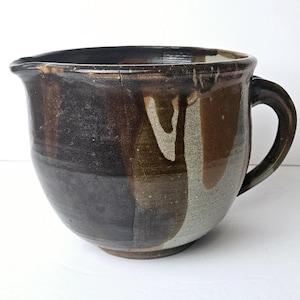 May include: A large, brown and white ceramic mixing bowl with a handle. The bowl has a rustic, handmade look and is glazed in a mottled brown and white pattern.