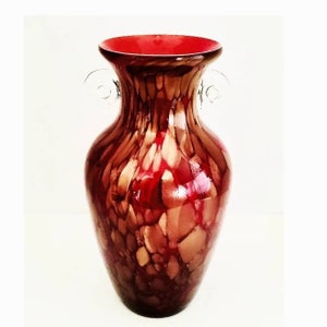 Può includere: Un vaso di vetro rosso e marrone con un motivo screziato e due manici. Il vaso ha un'apertura larga e una base stretta.