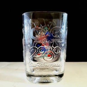 May include: Clear glass tumbler with a frosted design featuring the Walt Disney World logo and the year 2000. The design includes a Mickey Mouse silhouette and other celebratory imagery.