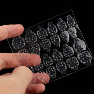 May include: A clear plastic sheet containing twenty-four individual adhesive nail tabs arranged in various sizes. Each tab features a rounded rectangular shape with a small pull tab at the base and a grid pattern embossed on the adhesive surface.