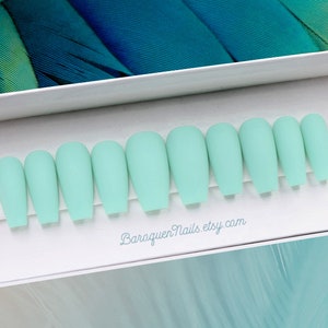 May include: A set of ten matte mint green press-on nails arranged in a row on a white display card. The nails feature a coffin shape with a smooth, non-reflective finish. The text BaroquenNails.etsy.com is printed in light blue below the nails.