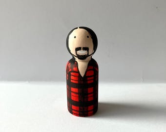 May include: A wooden peg doll with a black beard and hair, wearing a red and black plaid shirt.