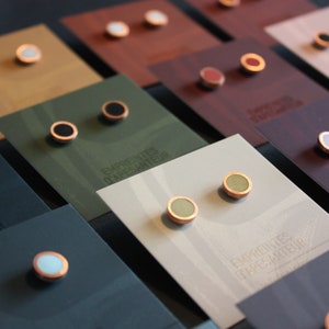 Op de afbeelding: Een display met kleine ronde oorbellen met verschillende gekleurde stenen en koperen settings. De oorbellen worden gepresenteerd op kaarten met de tekst "Empreintes d'Artisan" erop gedrukt.