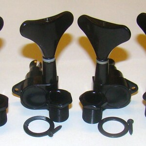 May include: Four black bass guitar tuning keys with a wing-shaped design. Each key has a black plastic base and a silver metal shaft.