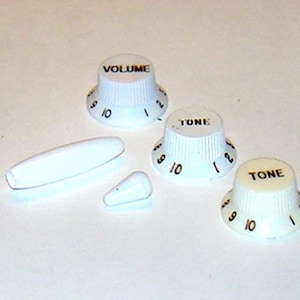 May include: Four white guitar knobs with black lettering. Two knobs say "TONE" and two knobs say "VOLUME". The knobs have numbers 1-10 on them. There is also a white guitar knob with a white tip.