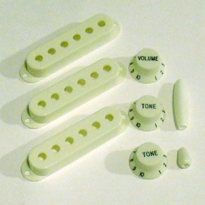 May include: Off-white guitar pickup covers, volume and tone knobs, and a switch tip. The pickup covers have seven holes. The knobs are labeled "VOLUME" and "TONE" with numbers 1-10. A guitar parts set.