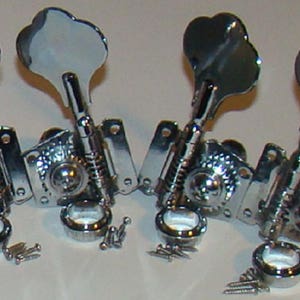May include: Four chrome bass guitar tuning keys with a vintage style. The keys are in a row and have a silver finish.