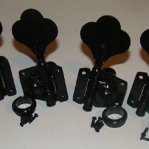 May include: Four black bass guitar tuning keys with a heart-shaped design. The keys are attached to a metal plate with screws.