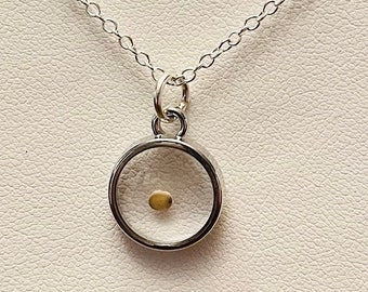 May include: A silver necklace with a round pendant containing a single, small, yellow seed.
