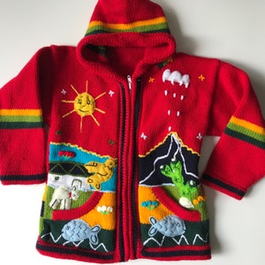 Puede incluir: Suéter rojo de punto con capucha y detalles bordados de colores, incluyendo un sol, un pájaro, una montaña y un cactus. El suéter tiene una cremallera y dos bolsillos.
