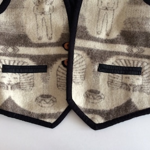 Peut inclure: Un gilet crème avec une bordure noire et un motif brun. Le gilet a deux poches sur le devant et une fermeture à bouton.
