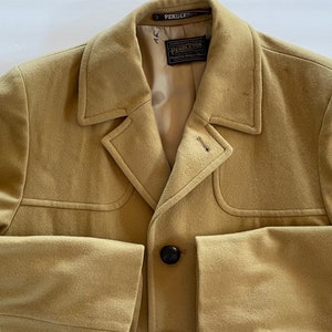 May include: A tan wool coat with a single button closure and a Pendleton label. The coat has a notched collar and a welt pocket on the left side.