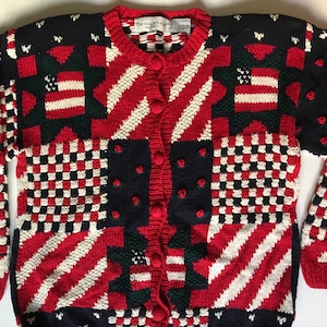 May include: A red, white and blue cardigan sweater with a patchwork design. The cardigan has a button fastening and is made of a soft, knitted fabric. The Eagles Eye label is visible on the collar.
