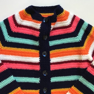 Puede incluir: Cárdigan de crochet hecho a mano, colorido, con base azul marino y rayas vibrantes en naranja, rosa, blanco y turquesa. El suéter con botones presenta un cuello alto y botones oscuros, perfecto para un look acogedor y elegante.