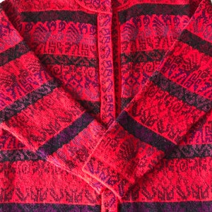 May include: Red cardigan with a geometric pattern in black and purple. The cardigan has a button closure and a high neckline.