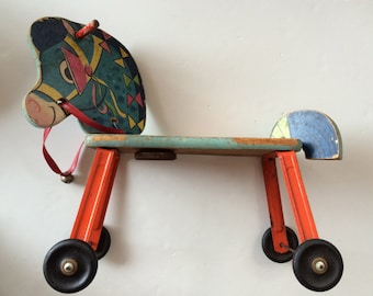 May include: A vintage wooden rocking horse toy with a blue, green, and yellow painted design. The horse has red wheels and a red bridle.