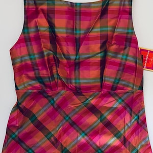 May include: A sleeveless top featuring a vibrant plaid pattern in shades of magenta, orange, teal, and dark purple. The garment has a boat neckline and a fitted bodice with vertical seams. A small yellow tag with the text ISAAC MIZRAHI is attached.