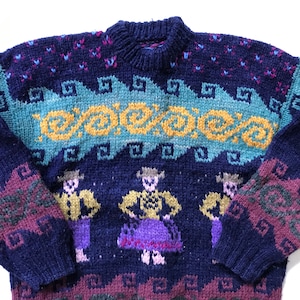 May include: A navy blue jumper with a crew neck and long sleeves. The jumper features a colourful pattern with teal, yellow, purple, and burgundy accents. The design includes stylized figures and geometric shapes.