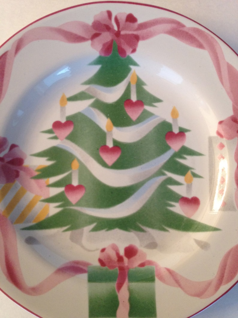 Op de afbeelding: Een wit keramiek bord met een groen kerstboomontwerp. De boom is versierd met roze harten, witte kaarsen en roze linten. Een groene cadeaudoos met een roze strik bevindt zich onderaan het bord.