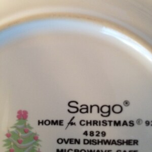 Op de afbeelding: Een wit keramiek bord met een kerstboomontwerp en de tekst "Sango&reg; HOME for CHRISTMAS&reg; 92 4829 OVEN DISHWASHER MICROWAVE SAFE INDONESIA".