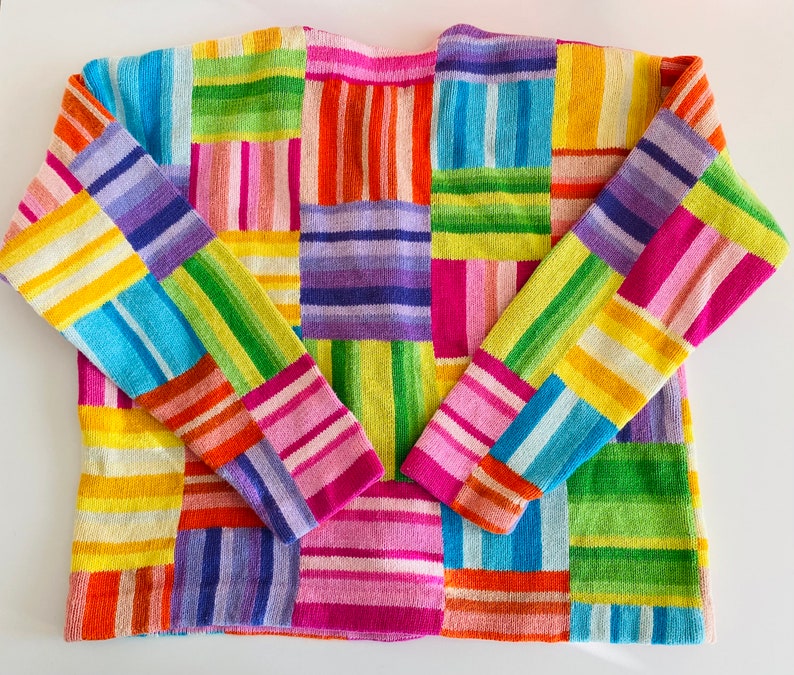 May include: A colorful knitted sweater with a patchwork design featuring stripes of pink, blue, green, yellow, and purple.