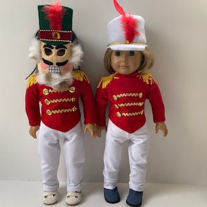 May include: Two dolls dressed as toy soldiers. One doll is wearing a red and gold uniform with a nutcracker mask. The other doll is wearing a red and gold uniform with a white hat and red feather.
