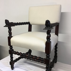 May include: A white upholstered armchair with a dark wood frame. The chair has a twisted design on the legs and arms, and the arms are topped with carved lion heads.