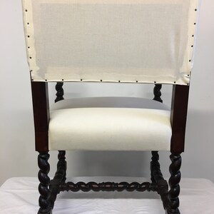 May include: A white upholstered chair with a dark wood frame. The chair has a twisted, carved design on the legs and a square back.