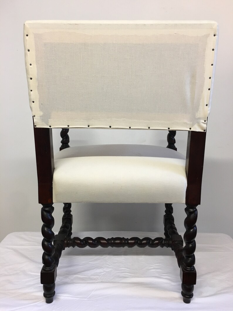 May include: A white upholstered chair with a dark wood frame. The chair has a twisted, carved design on the legs and a square back.