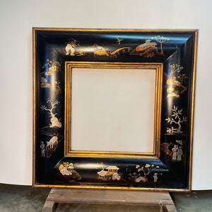 May include: A black picture frame with gold accents and a decorative design of Asian-inspired scenes. The frame is made of wood and has a rectangular shape.