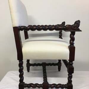 May include: A dark wood chair with a white upholstered seat and back. The chair has a twisted design on the legs and arms, and the arms are finished with carved lion heads.