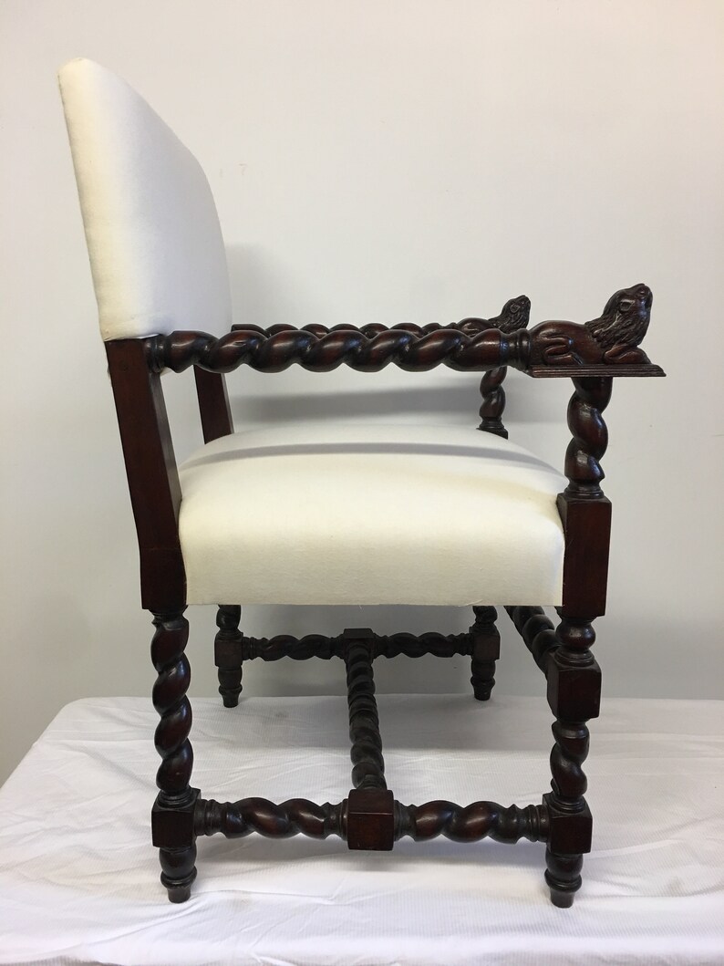 May include: A dark wood chair with a white upholstered seat and back. The chair has a twisted design on the legs and arms, and the arms are finished with carved lion heads.