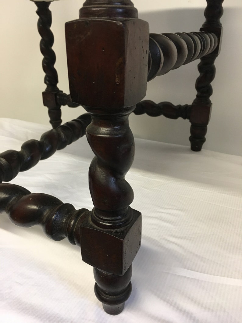 May include: Close-up of a dark brown wooden table leg with a twisted design. The leg is square at the top and bottom, with a rounded, twisted section in the middle.