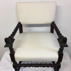 May include: A white upholstered armchair with a dark wood frame. The chair has a twisted design on the arms and legs, and the arms are topped with carved lion heads.