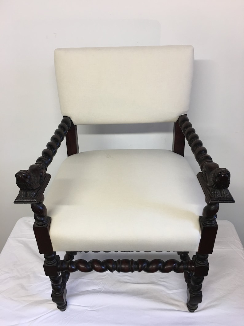 May include: A white upholstered armchair with a dark wood frame. The chair has a twisted design on the arms and legs, and the arms are topped with carved lion heads.