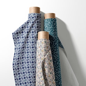 Pode incluir: Três rolos verticais de tecido com padrões distintos. Um rolo é azul-escuro com motivos de linhas circulares brancas, outro é bege-claro com padrões circulares multicoloridos e o terceiro é azul-petróleo com pequenas formas florais brancas.