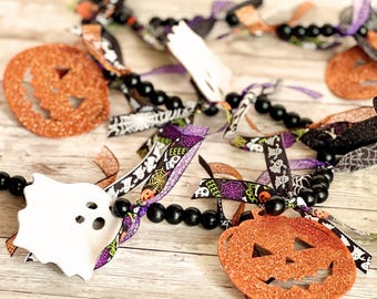 May include: A Halloween garland with black beads, orange and white felt pumpkins and ghosts, and purple, black, and white ribbon with a spooky pattern.