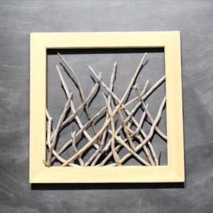 May include: A framed artwork featuring a collection of light brown twigs arranged in a random pattern against a dark gray background.