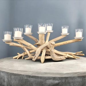 Peut inclure: Un bougeoir rustique en bois flotté avec six bougeoirs en verre. Le bougeoir est posé sur une surface en béton gris.